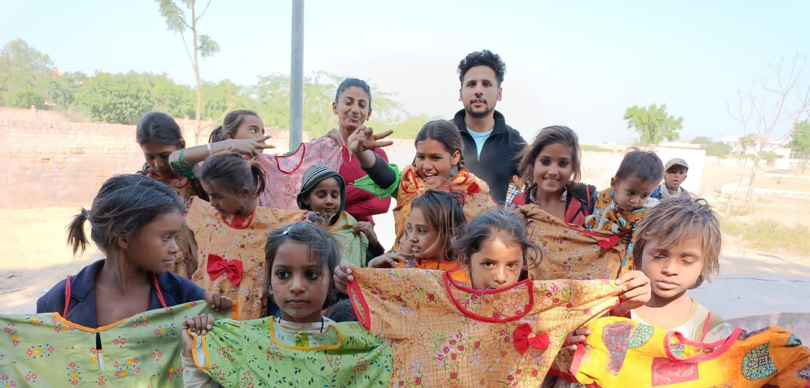 Slum kids holding up colourful frocks stitched by women in the STARK Foundation stitching program, on Children's Day 2021
